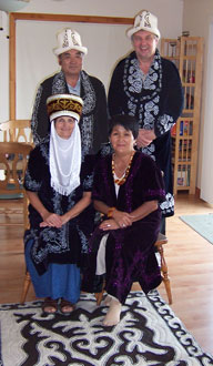 The parents in traditional Kyrgyz dress in front of a traditional Kygyz rug
