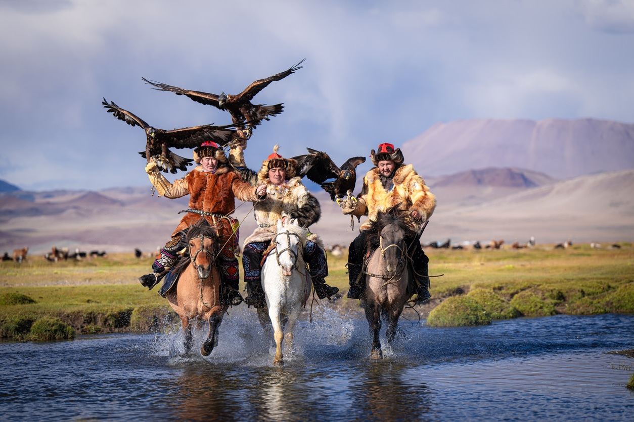 group of Kazakh eagle hunters riding horses crossing river