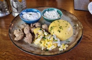 Traditional Moldovan food, meal closeup with pork stew, mamaliga polenta, fried eggs, cheese and sour cream sprinkled with parsley